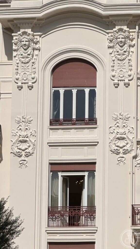 A tall arched window flanked by two stucco heads and decorative panels