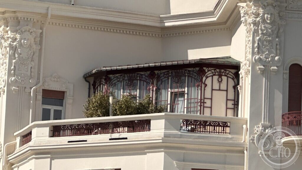 A curved veranda of iron and glass set into the corner of the hotel above a balcony