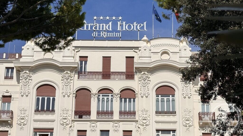 The upper floors of the hotel with the roof sign and flags, seen through branches