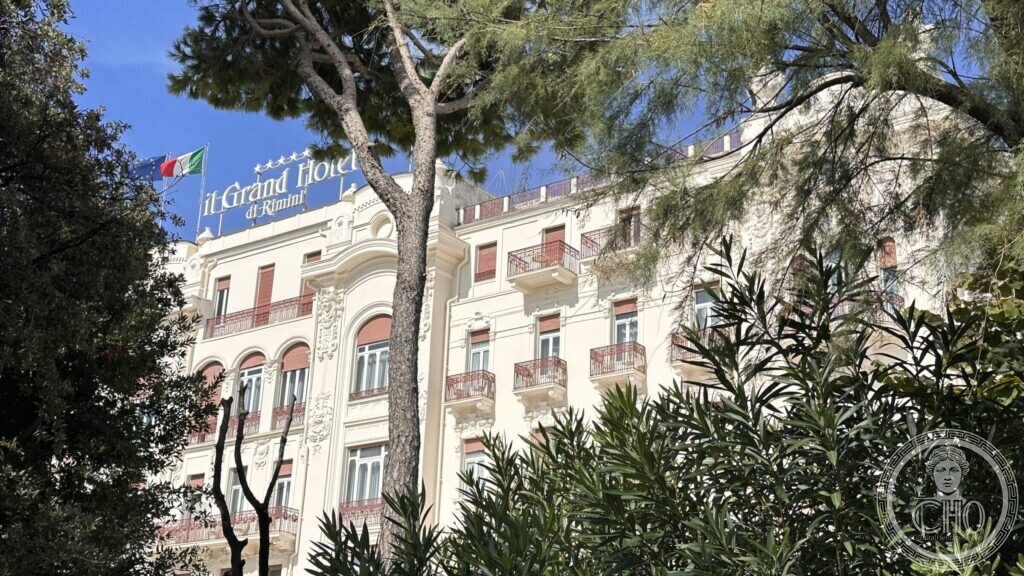 The roof sign reading Grand Hotel di Rimini, framed by umbrella pines
