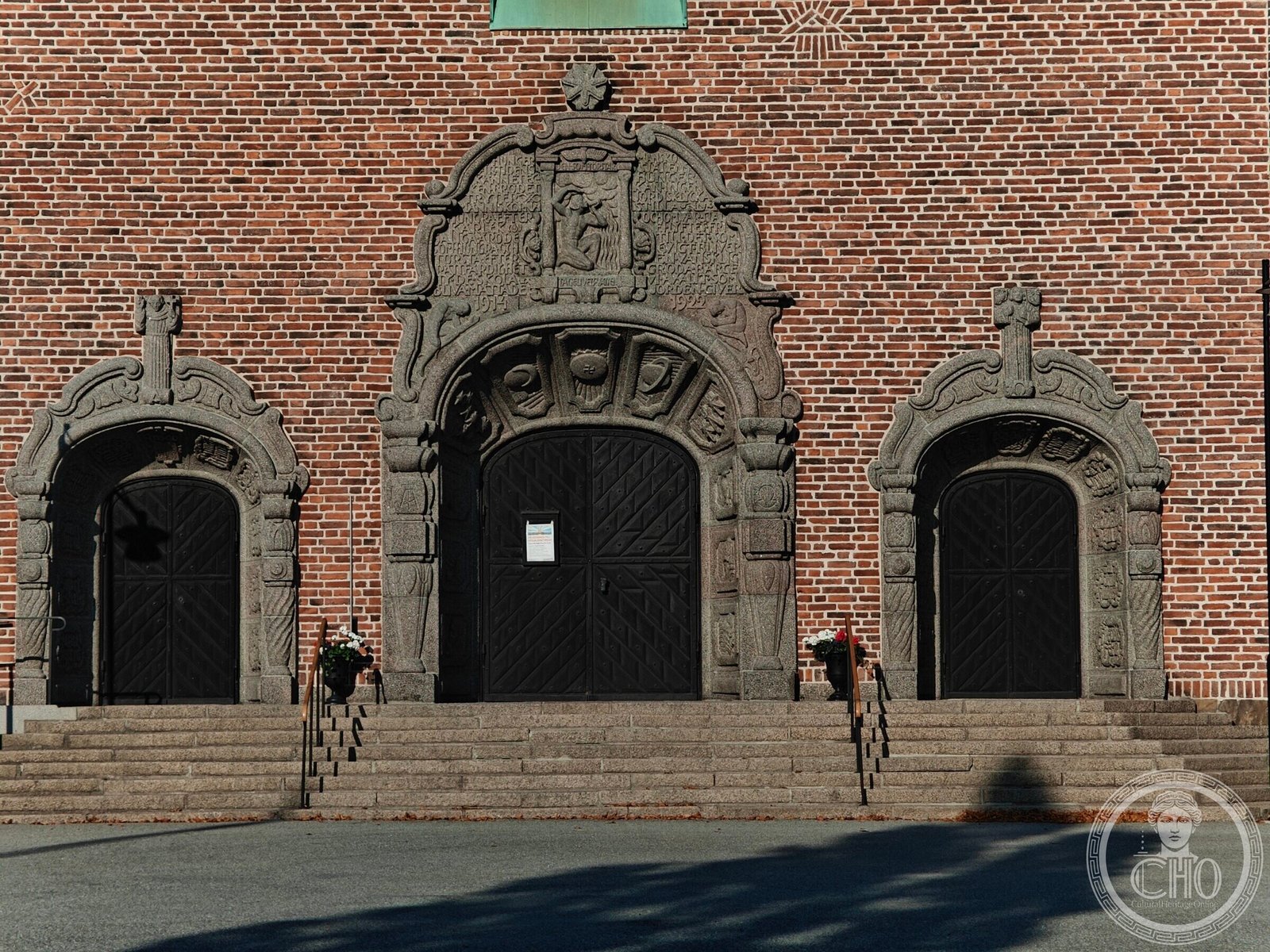 The three carved granite doorways of Högalidskyrkan's west entrance, set in dark red brick above a broad flight of steps