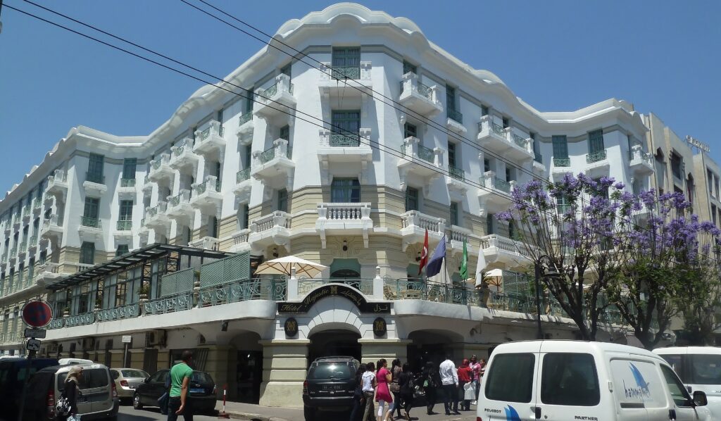 White Art Nouveau facade of the Hôtel Majestic on Avenue de Paris, Tunis, with a wave-shaped roofline, stacked balconies with green iron railings and a first-floor terrace