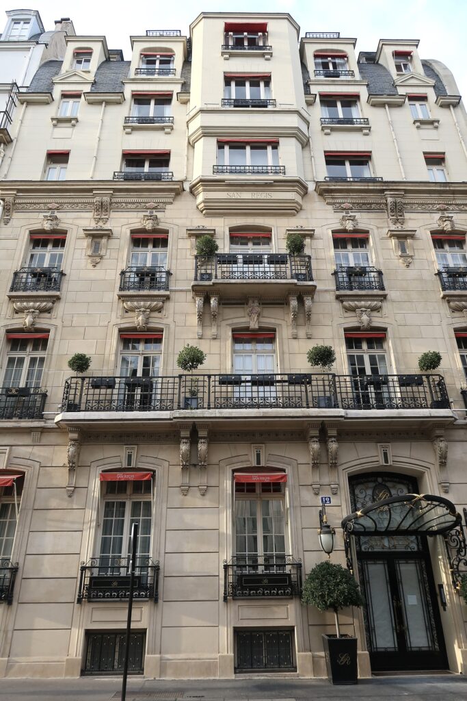 Stone façade of the Hôtel San Régis at 12 rue Jean-Goujon, Paris, with a long wrought-iron balcony on carved consoles, a frieze, and a central bay window lettered San Regis on the upper floors