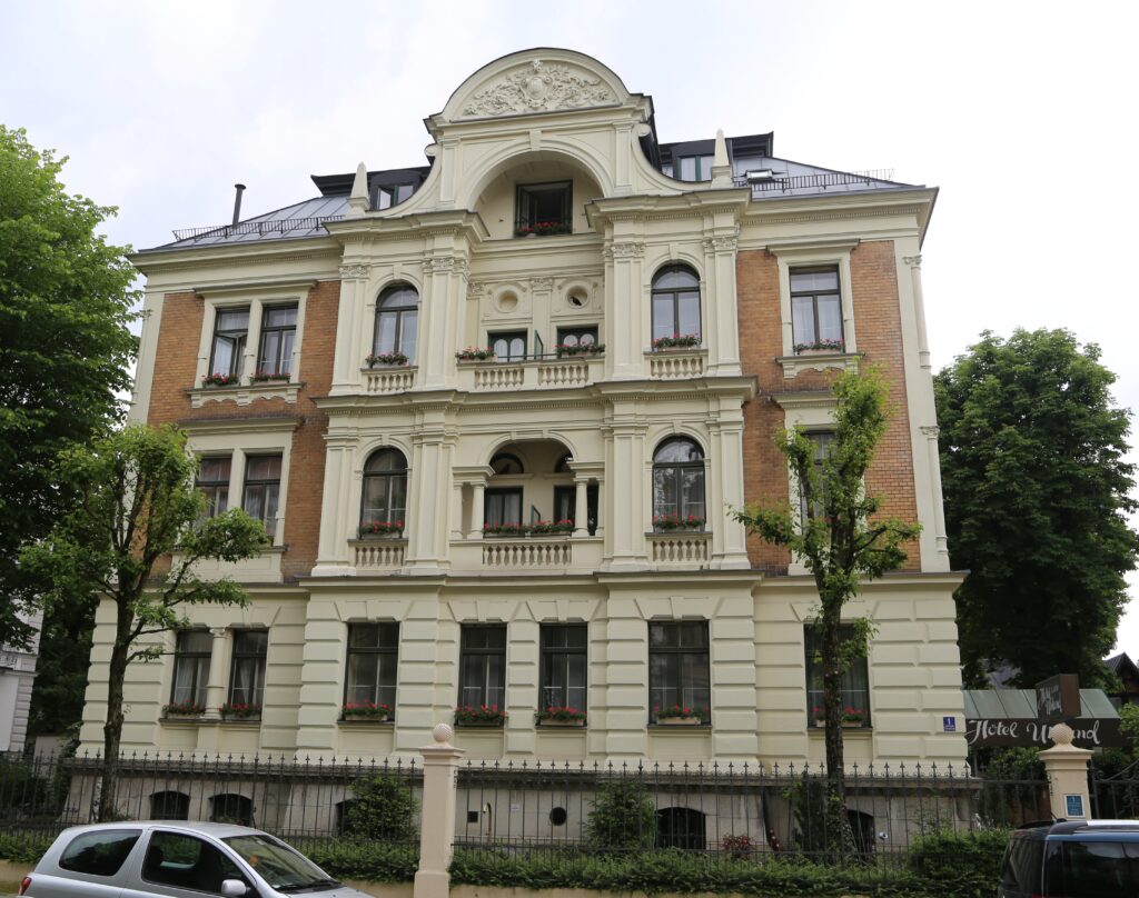 Neo-Renaissance house at Uhlandstraße 1, Munich: cream stucco central bay with arched windows, balustraded balconies and a curved gable, between brick-faced side bays