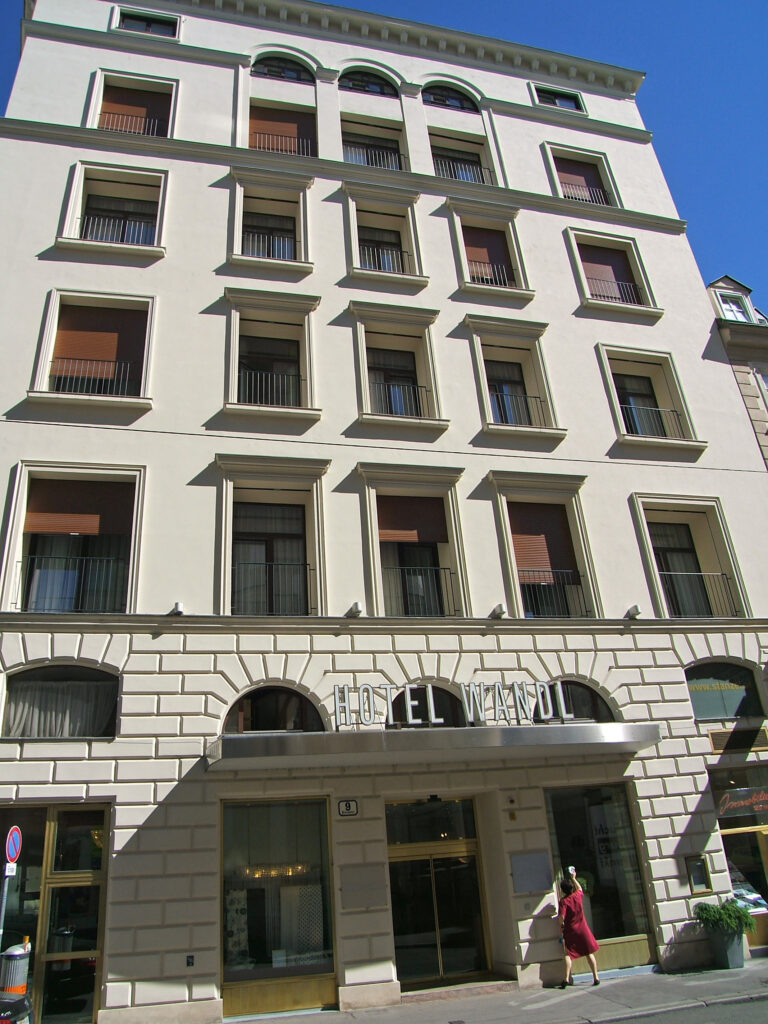 Tall cream corner building with a rusticated arched ground floor and the letters HOTEL WANDL above the entrance canopy, Petersplatz, Vienna