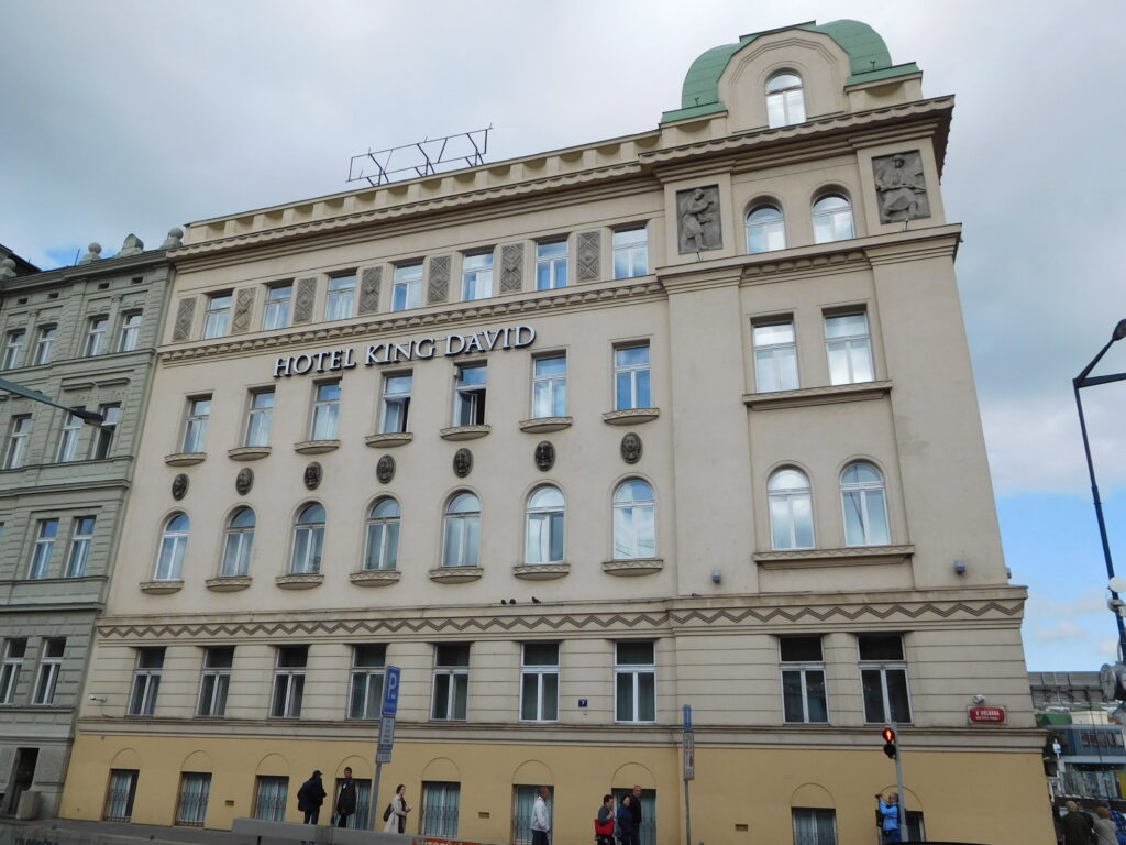 Cream corner building at Hybernská 42 in Prague crowned by a green copper dome, with figural reliefs and oval medallions on the facade
