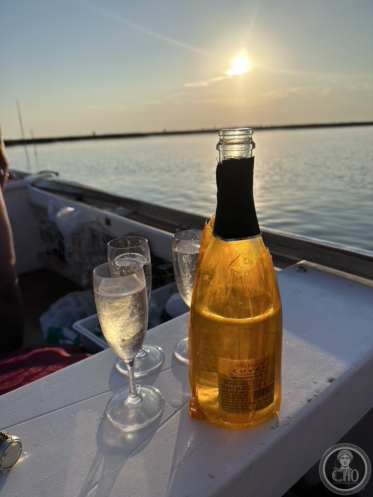 Chilled bottle of sparkling wine and glasses on the gunwale of a boat at sunset in the northern Venetian Lagoon