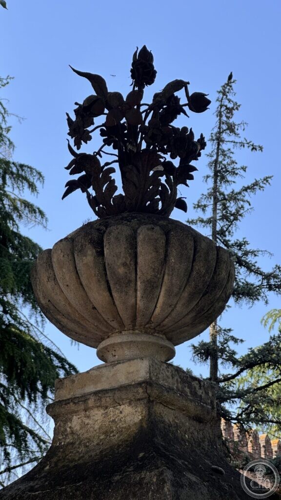 A carved stone urn on a gate pier, holding a bouquet of stone flowers, against the sky