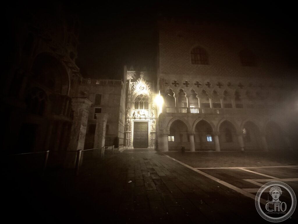 The Porta della Carta and the ground-floor arcade of the Doge's Palace in fog at night, seen across the paving of the Piazzetta