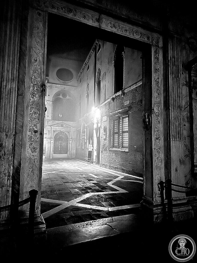 Looking through a carved marble doorway into the courtyard of San Giovanni Evangelista at night, in black and white