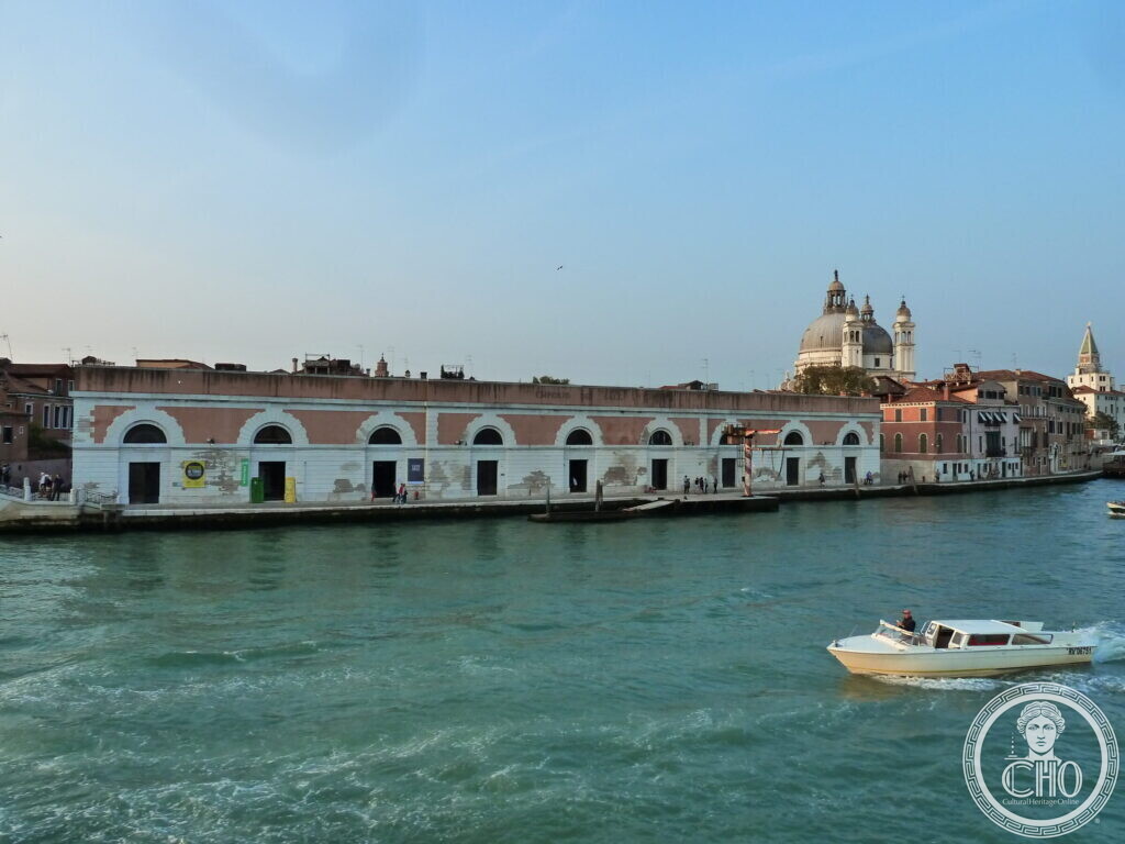 The long two-tone front of the salt warehouses with white arched openings along the water, a motorboat in the foreground and the Salute dome behind
