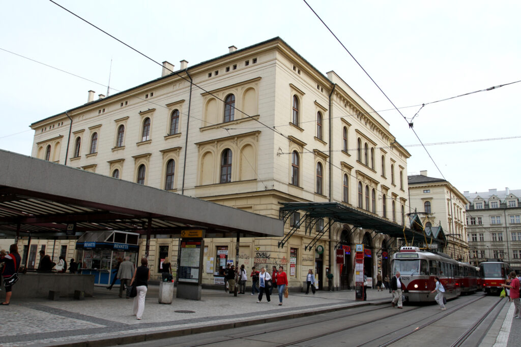 Cream classicist station building of Masarykovo nádraží in Prague with a glass canopy over the pavement and a tram stop in front