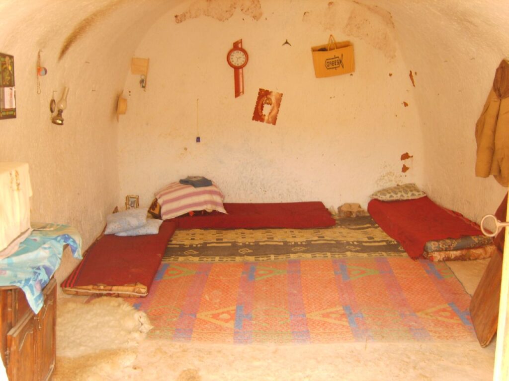 A carved bedroom inside a Matmata troglodyte house, with mattresses on the floor, a wall clock and personal belongings