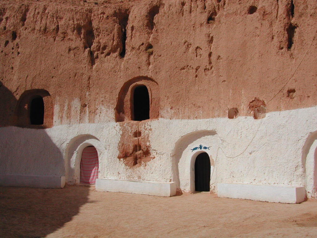 Interior courtyard of a Matmata troglodyte pit-house, with whitewashed carved rock walls, arched doorways and a painted fish motif