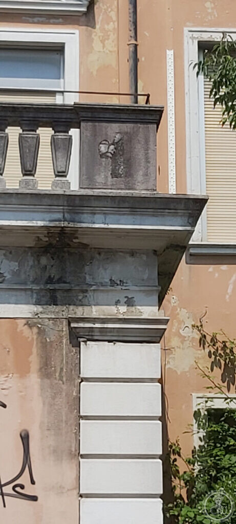 A close view of a pilaster and cornice on the Padiglione Cecchini in Mestre, with the plaster peeling away and a defaced relief panel