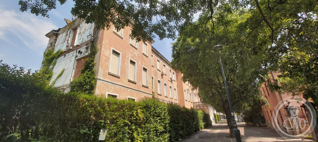 The long flank of the Padiglione Cecchini in Mestre seen along the street, its plaster falling away and ivy growing over the torn wall
