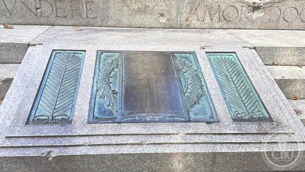 A green-patinated bronze tablet flanked by panels of bronze palm fronds, set into pink granite steps