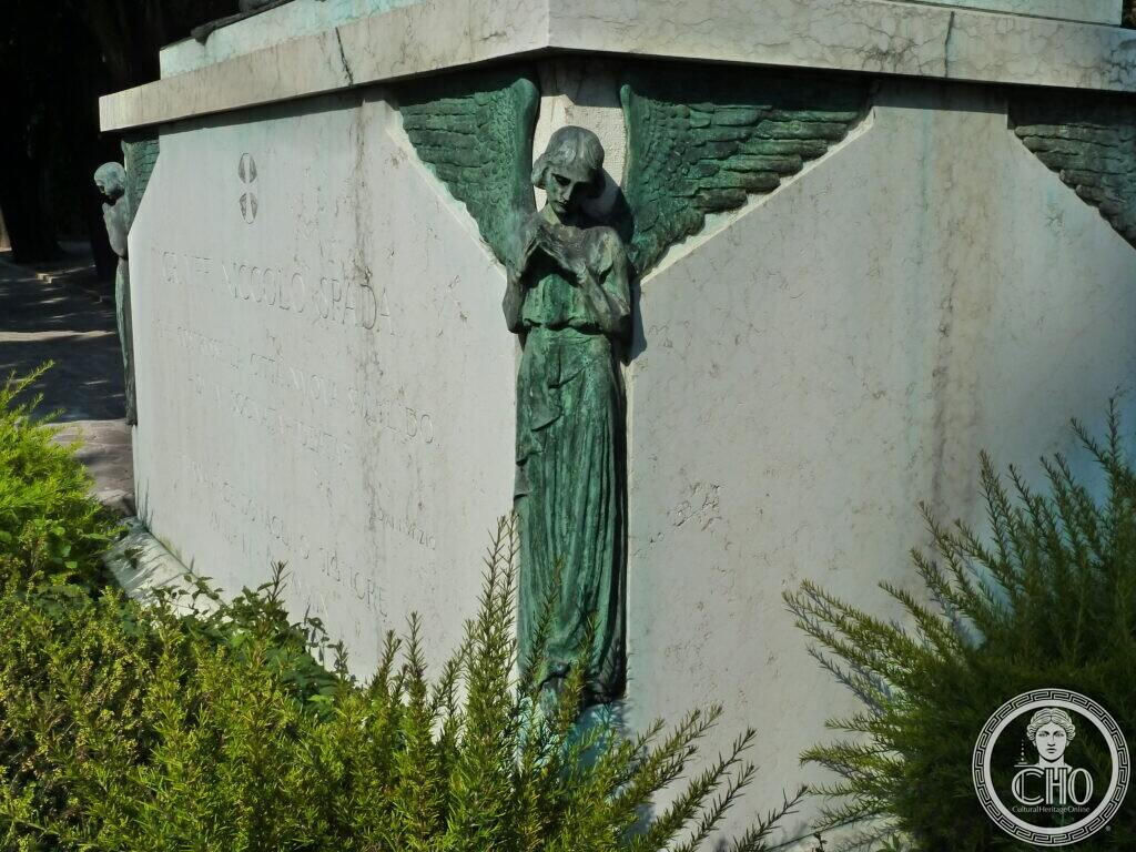One of the winged bronze angel figures at the corner of the tomb, beneath the inscription