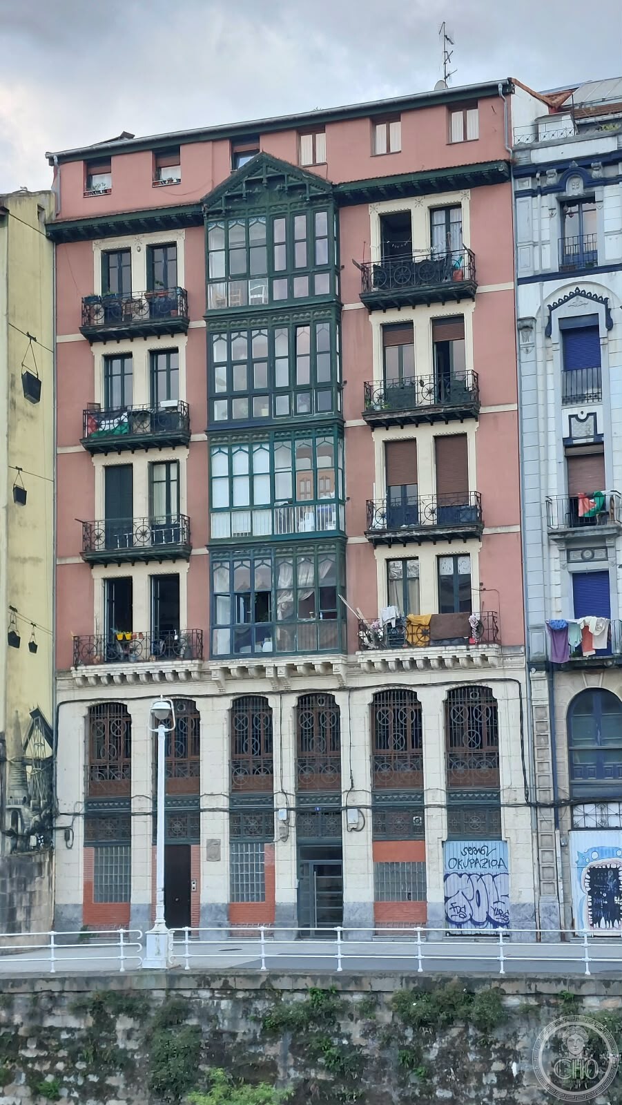 A pink building facade with a tall green-framed glass gallery, on the Muelle de Bilbao la Vieja, Spain