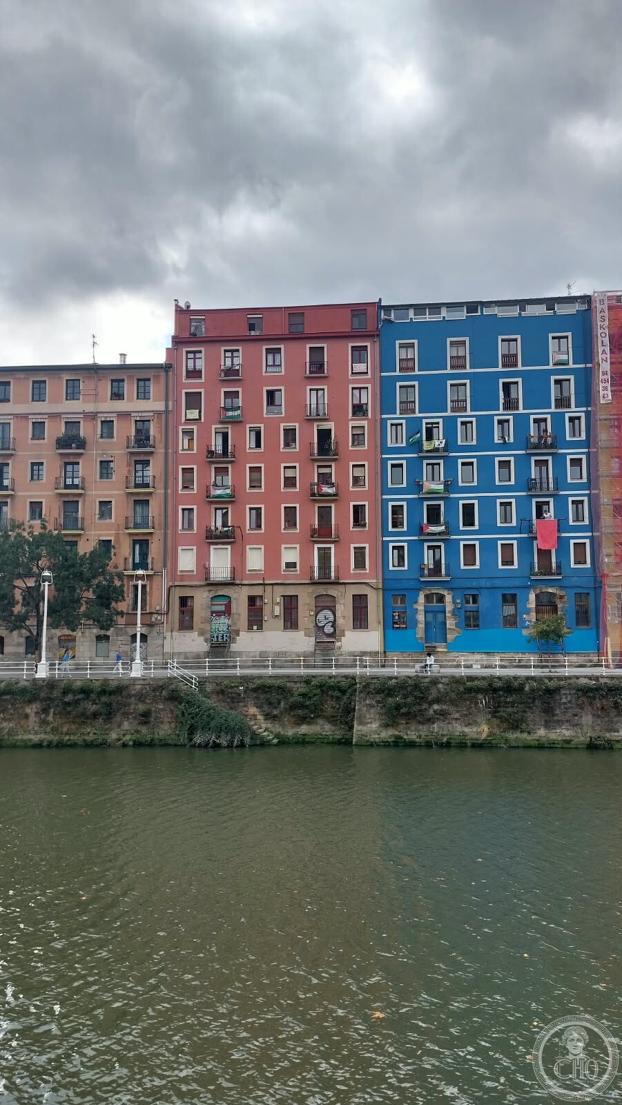 Row of colourful pink and blue apartment facades along the Muelle de Bilbao la Vieja, with Palestinian flags on balconies