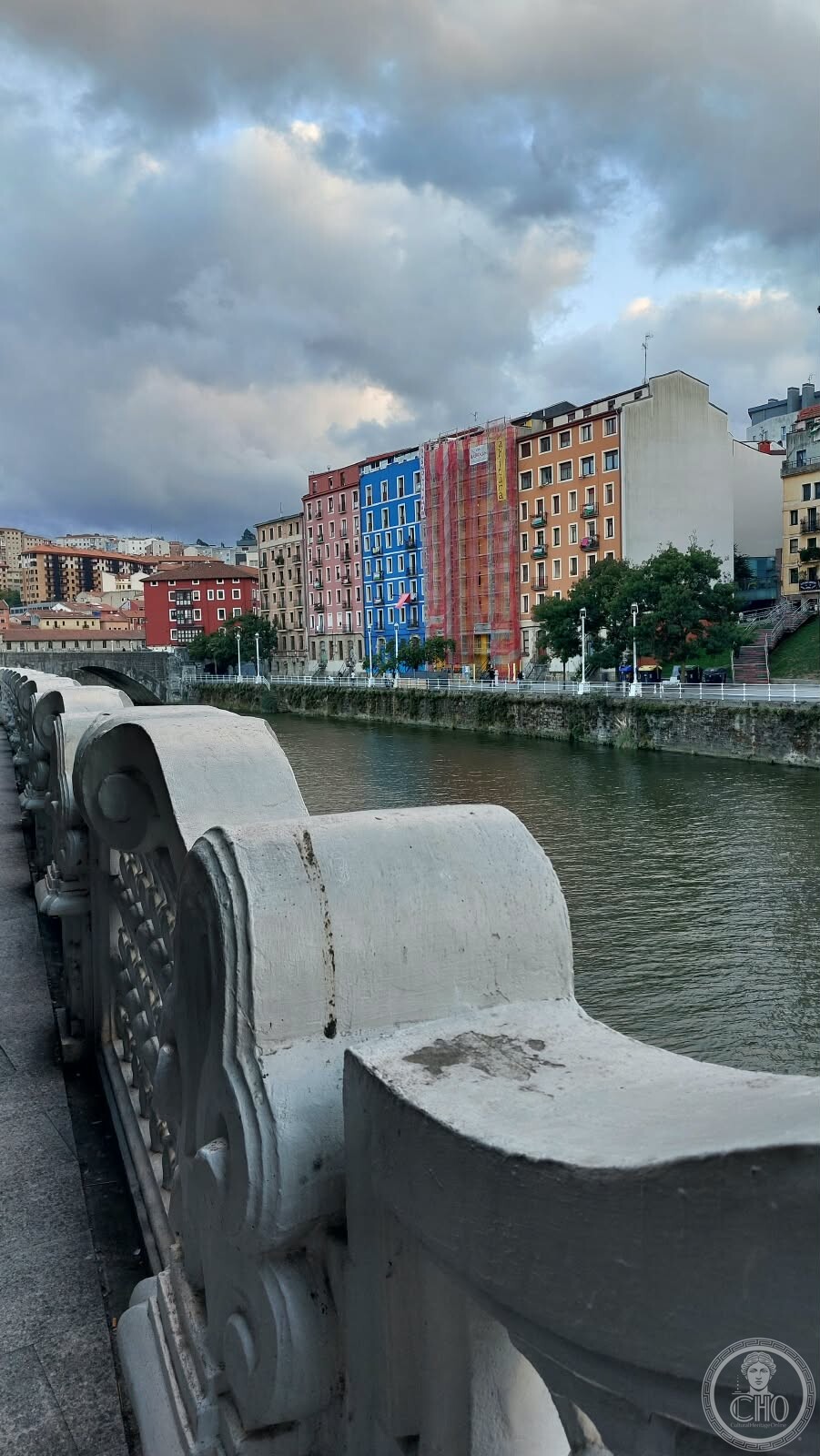 View along the Nervion river toward colourful facades on the Muelle de Bilbao la Vieja, seen from a stone bridge balustrade