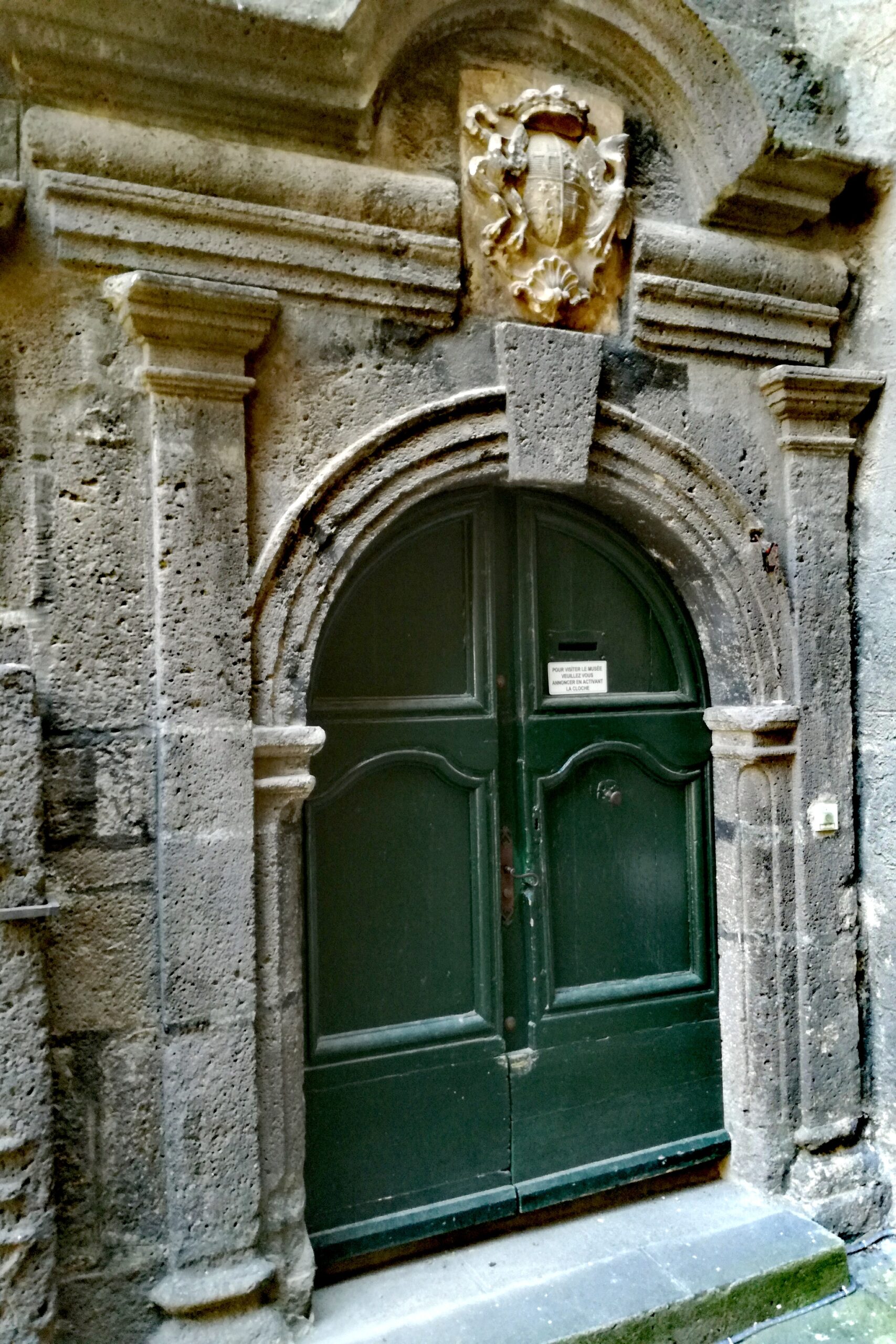 A Renaissance stone doorway in dark volcanic stone with a carved coat of arms above a green double door