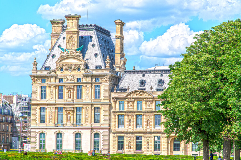 South front of the Pavillon de Marsan, Louvre, Paris: pale stone pavilion with steep slate roof, tall chimneys, statues in niches and a winged sculpture on the pediment, seen from the Tuileries