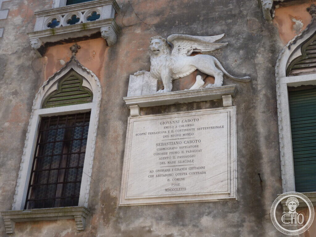 A marble plaque inscribed to Giovanni and Sebastiano Caboto under a carved winged lion, between two pointed Gothic windows