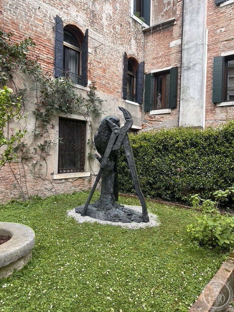 A giant bronze sculpture of pliers and a hammer by Jim Dine set on the lawn of the private garden of Palazzo Contarini degli Scrigni e Corfù, beside an old stone wellhead
