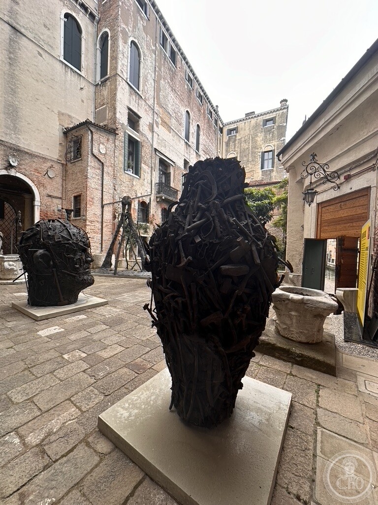 Two large bronze assemblage heads by Jim Dine standing in the brick-walled courtyard of Palazzo Contarini degli Scrigni e Corfù during the 2024 Biennale exhibition