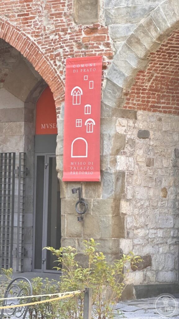 The entrance to the Museo di Palazzo Pretorio under a brick arcade, with a red banner