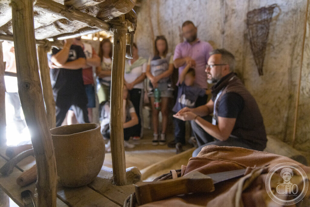 A guide shows prehistoric tools and pottery to visitors inside a reconstructed pile-dwelling at Livelet