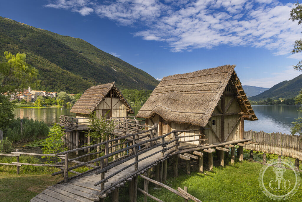 Two reconstructed pile-dwellings of the Livelet park on the shore of Lake Lago, with the village across the water
