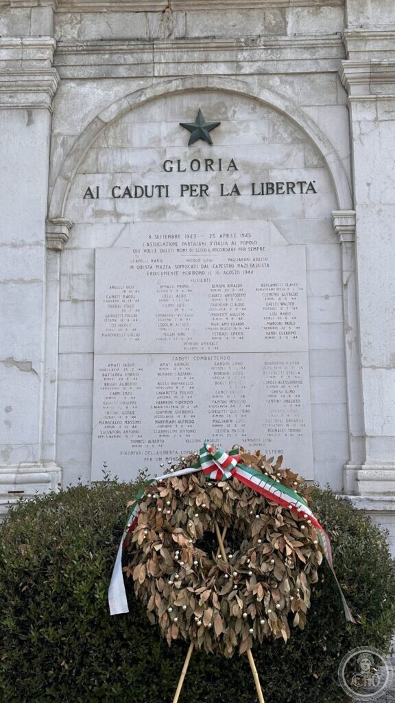 Marble memorial wall under the clock tower reading Gloria ai caduti per la liberta, with a laurel wreath below