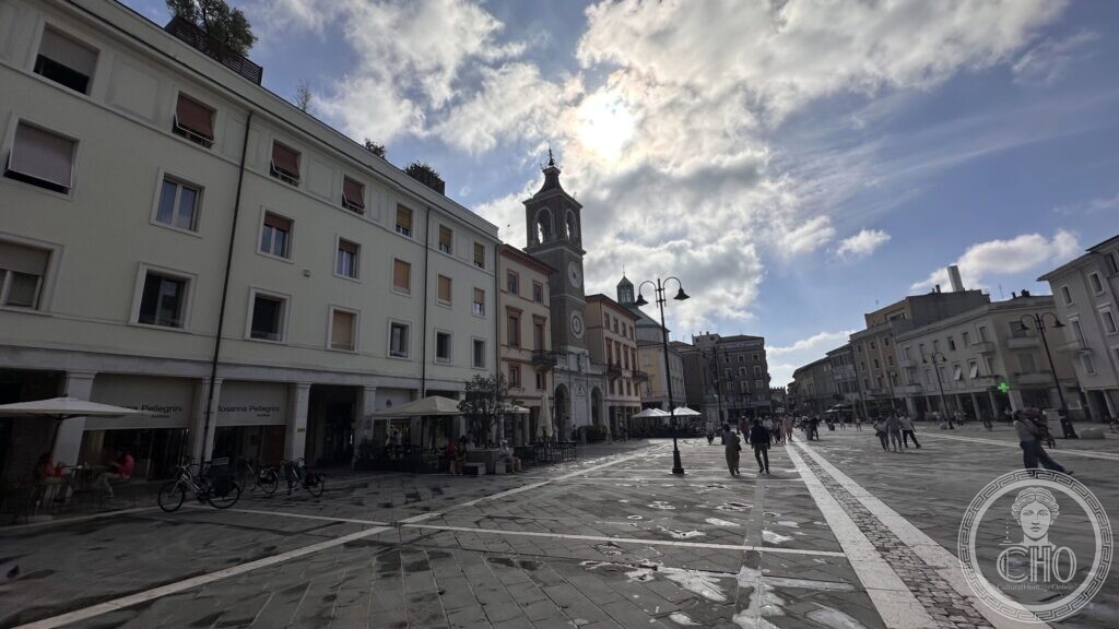 The long paved square with the clock tower on the left and the Arch of Augustus closing the view in the distance