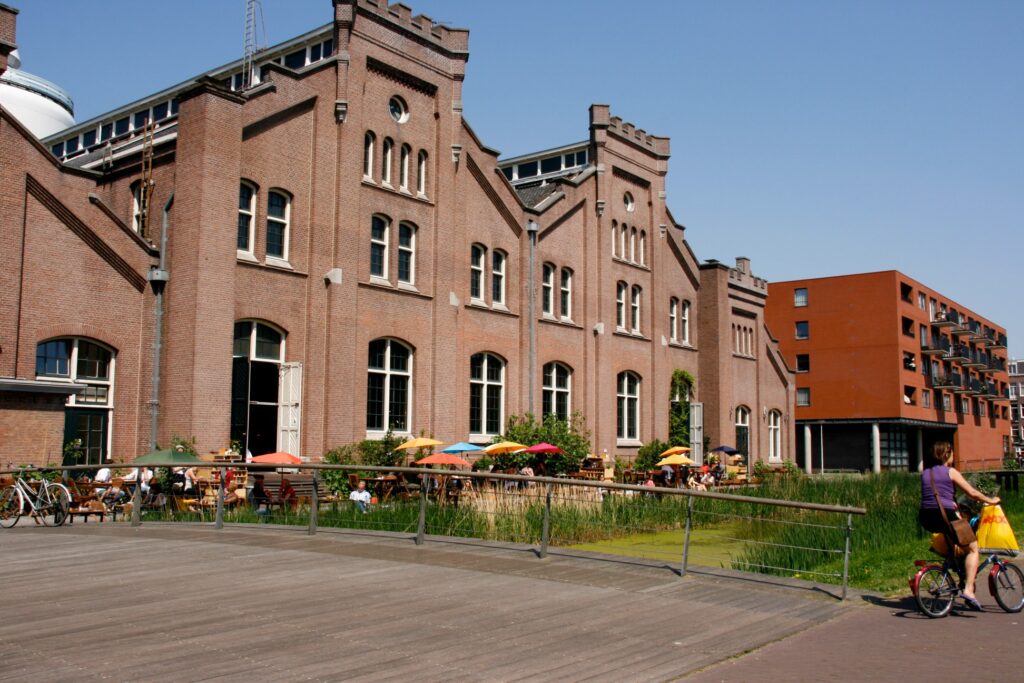 Red-brick halls of the former municipal water pumping station on Watertorenplein, Amsterdam, with crenellated gables, tall arched windows and a café terrace in front