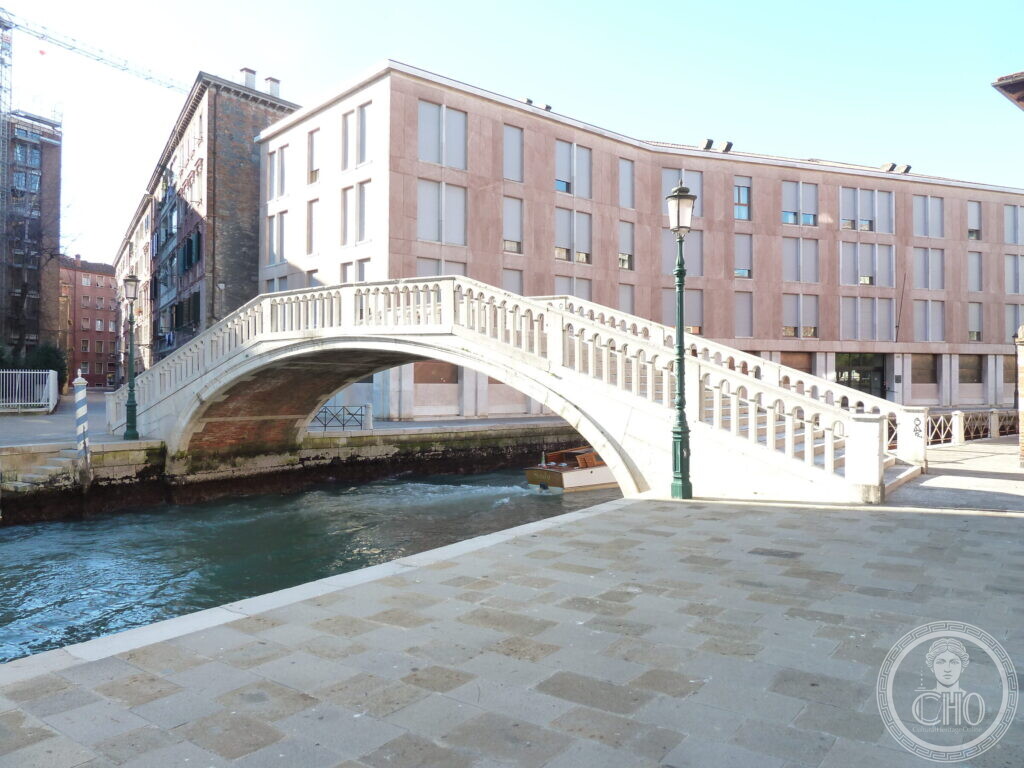 The Ponte de la Sbiaca seen from a wide stone quay, with a boat passing beneath