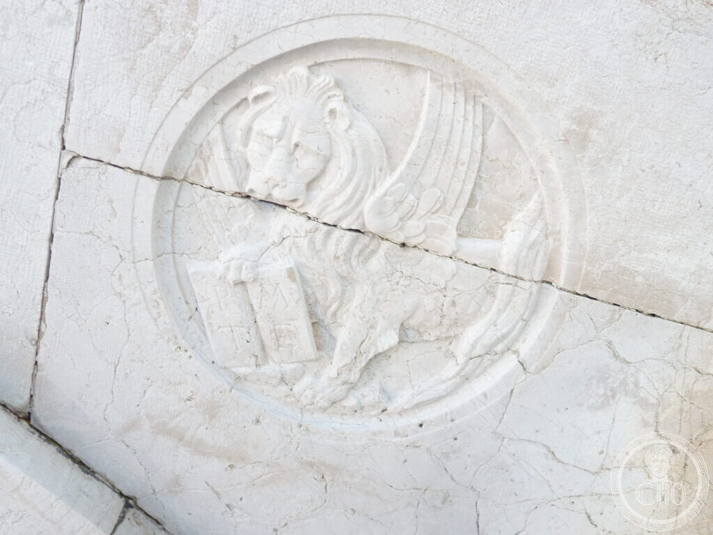A carved roundel of the winged lion of Saint Mark in white stone, crossed by a crack