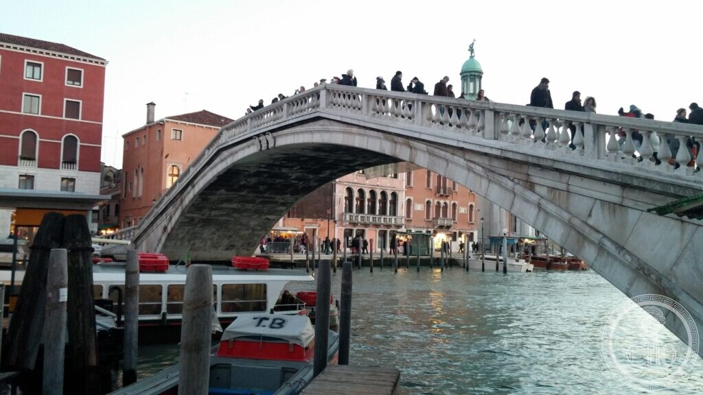 The stone arch of the Ponte degli Scalzi seen from a landing stage, with people crossing above