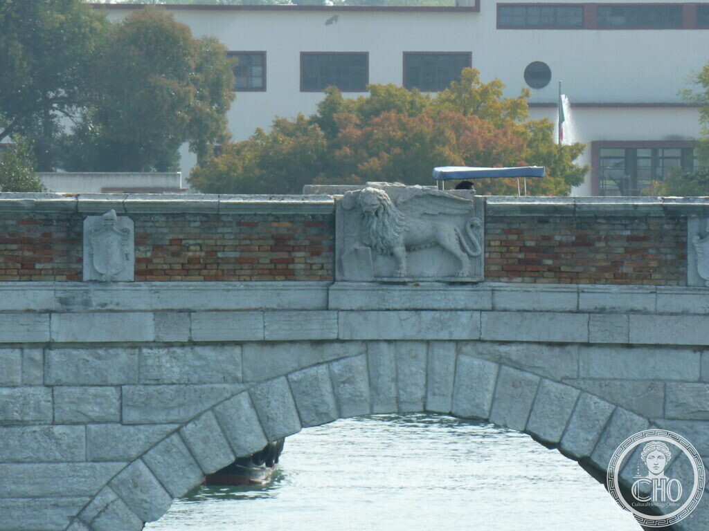 Close view of a carved stone winged lion with an open book set into the brick parapet of a bridge, a shield beside it
