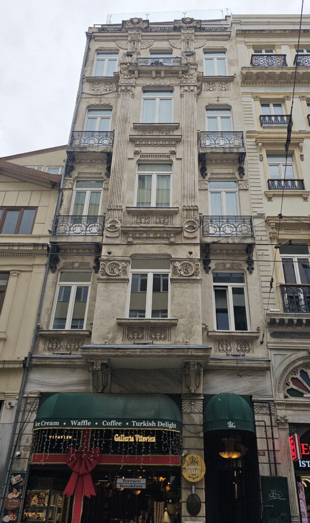 Narrow stone Art Nouveau facade of the Ravouna Building on İstiklal Avenue, Istanbul, with fluted pilasters, wrought-iron balconies, winged ornaments and RF monograms