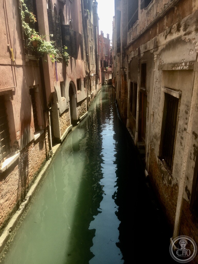 Scenic view down Rio di Santa Marina from Ponte dei Cavalieri showing weathered residential palace facades reflecting in green canal water