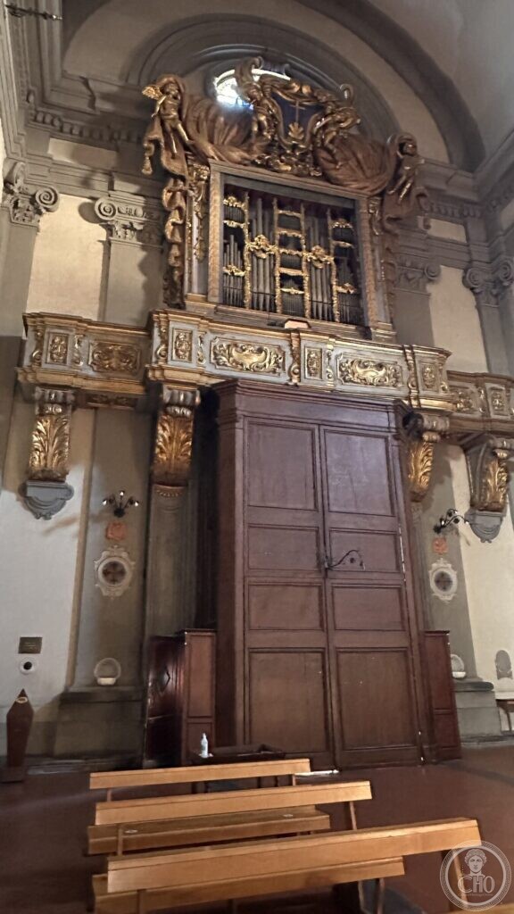 A baroque organ in a carved and gilded case above a gallery, with angels at the sides