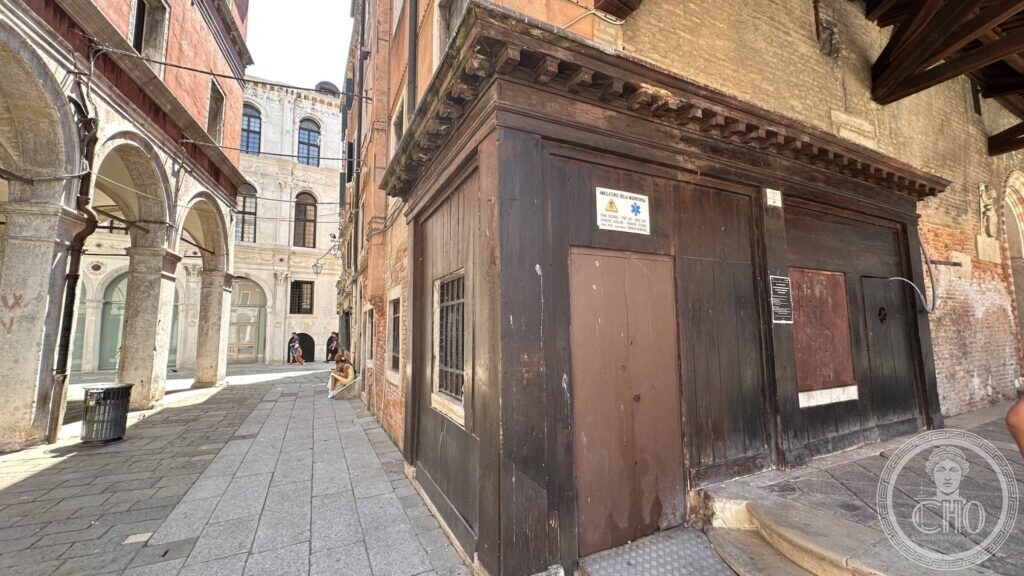 A timber structure against the flank of the church, with a first-aid sign in five languages above its door