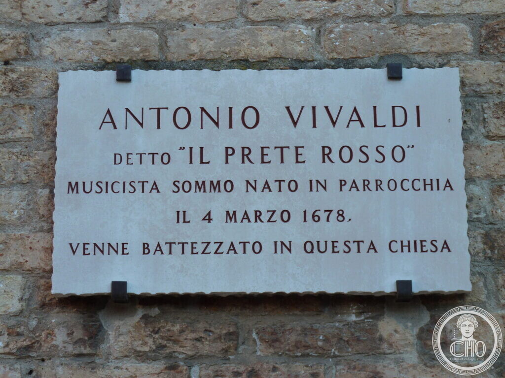 A white stone plaque with red lettering commemorating Antonio Vivaldi, known as the red priest, and his baptism in the church