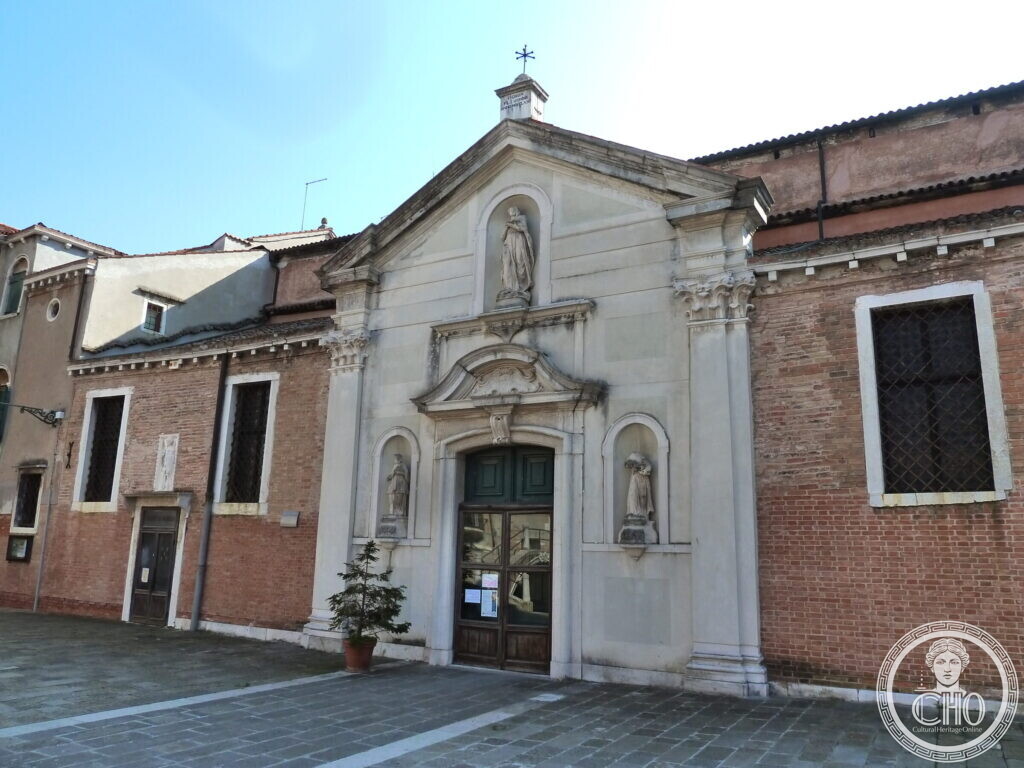 A white stone church doorway with statues in niches on each side and one above, set in a brick wall