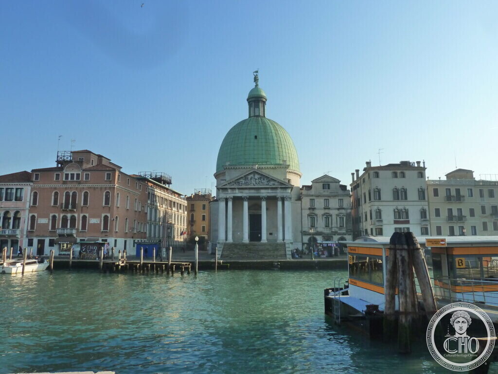 The domed church of San Simeone Piccolo seen across the Grand Canal between rows of houses, a water-bus stop in the foreground