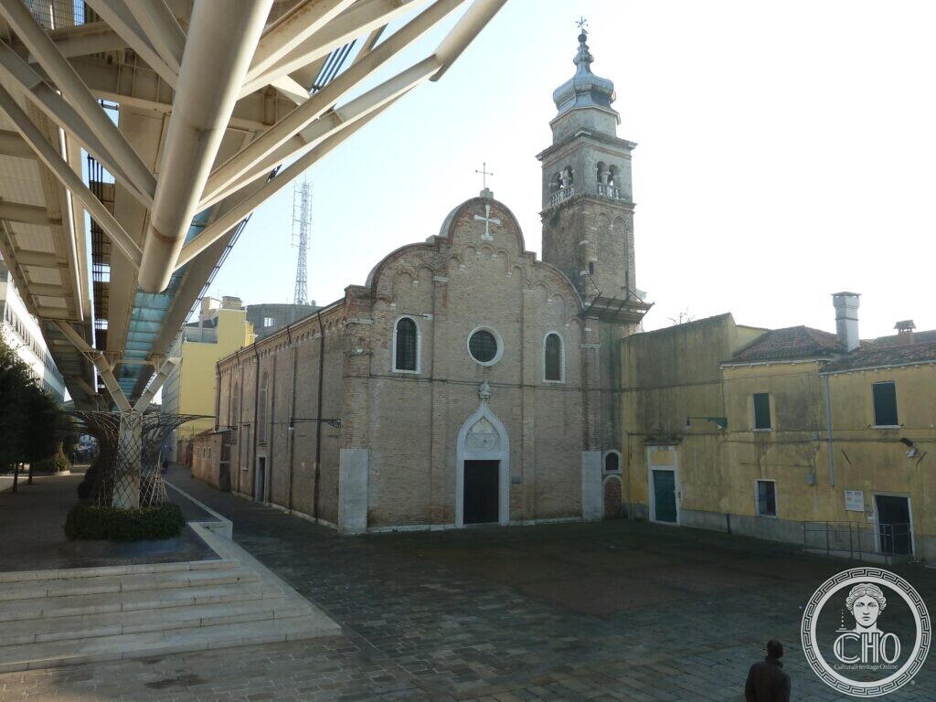 A Gothic brick church front with a round window and a pointed portal, a bell tower with an onion dome, and a steel elevated rail structure on the left