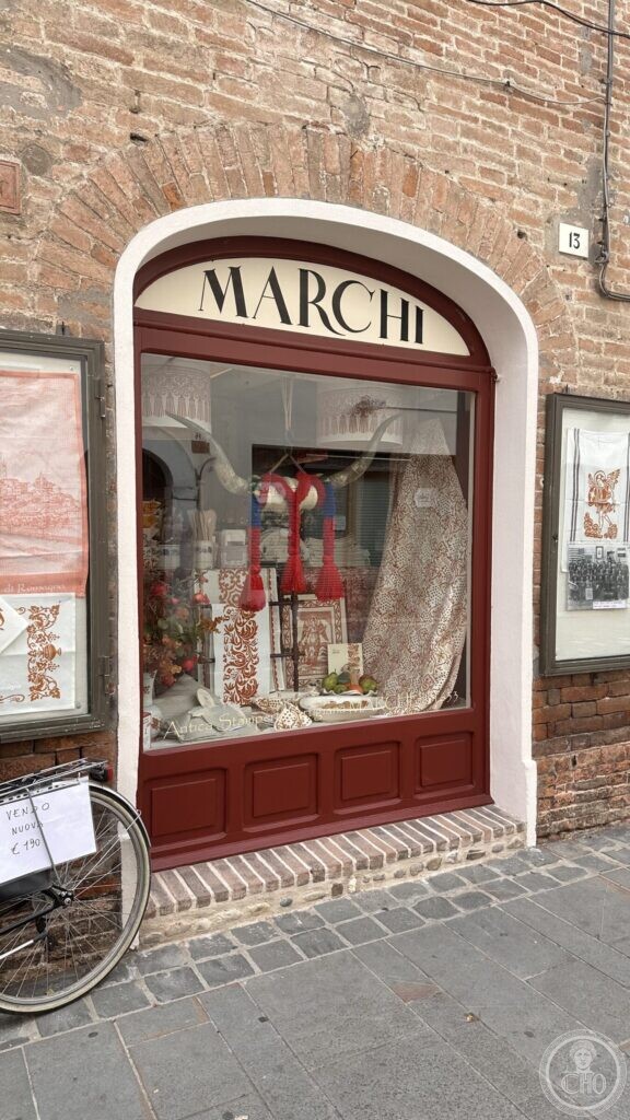 The shopfront of the Antica Stamperia Marchi in Santarcangelo di Romagna: a rounded window in a dark red frame with MARCHI in black capitals on the cream fanlight