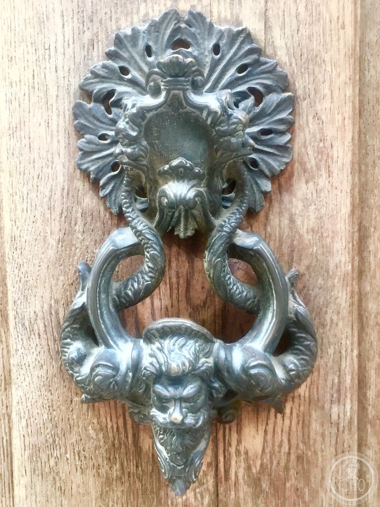 Detailed view of an ornate historic Venetian bronze door knocker depicting Neptune’s bearded face flanked by sea monsters on an antique timber door in Cannaregio